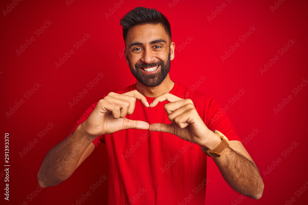 Sticker young handsome indian man wearing t-shirt over isolated red background smiling in love showing heart