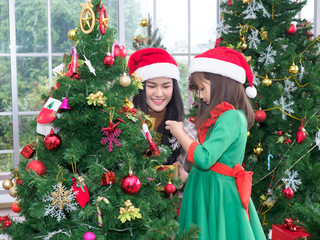 Portrait of happy girl wearing Santa cap and decorating gift box and Christmas tree at home. Young woman and a little cute girls are decorating for Christmas day.