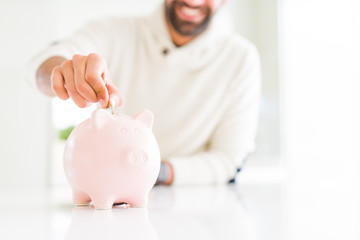Man smiling putting a coin inside of piggy bank saving for investment