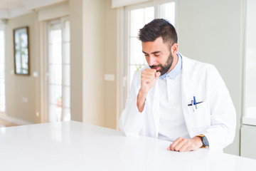 Fototapeta premium Handsome hispanic doctor or therapist man wearing medical coat at the clinic feeling unwell and coughing as symptom for cold or bronchitis. Healthcare concept.