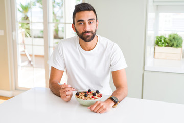 Handsome hispanic man eating healthy breakfast in the morning at home with a confident expression on smart face thinking serious