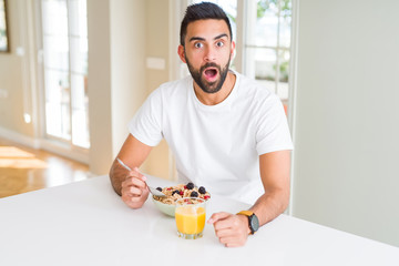 Handsome hispanic man eating healthy breakfast in the morning at home scared in shock with a surprise face, afraid and excited with fear expression