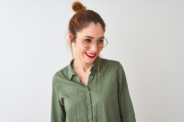 Redhead woman wearing green shirt and glasses standing over isolated white background looking away to side with smile on face, natural expression. Laughing confident.