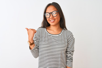 Young chinese woman wearing striped t-shirt and glasses over isolated white background smiling with happy face looking and pointing to the side with thumb up.
