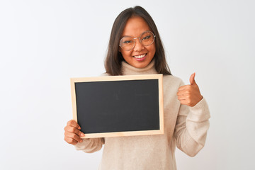 Young chinese woman wearing glasses holding blackboard over isolated white background happy with big smile doing ok sign, thumb up with fingers, excellent sign