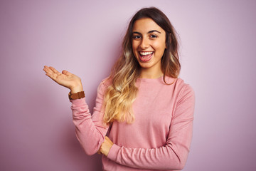 Fototapeta na wymiar Young beautiful woman wearing a sweater over pink isolated background smiling cheerful presenting and pointing with palm of hand looking at the camera.