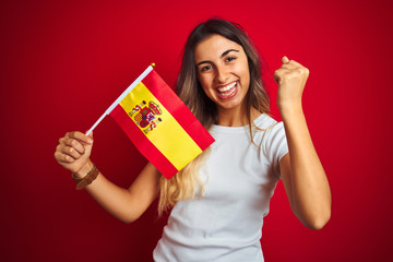 Young beautiful woman holding spanish flag over red isolated background screaming proud and...