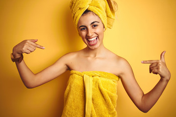 Young beautiful woman wearing a shower towel after bath over yellow isolated background looking...