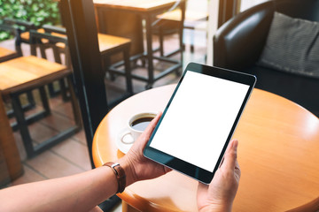 Mockup image of hands holding black tablet pc with blank white screen with coffee cup on wooden table