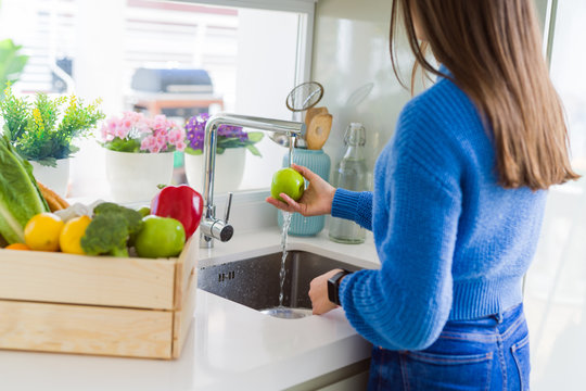 Young woman washing vegetables and fruit using water from sink