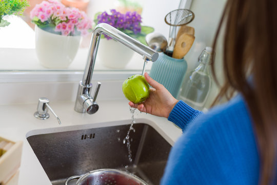 Young woman washing vegetables and fruit using water from sink