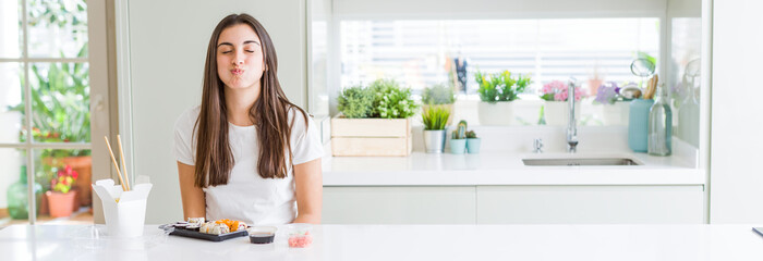 Wide angle picture of beautiful young woman eating asian sushi from delivery puffing cheeks with...