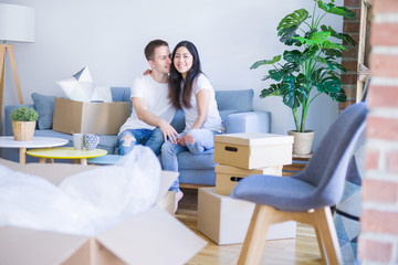 Young beautiful couple sitting on the sofa drinking coffee at new home around cardboard boxes