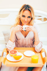 young beauty blond woman having breakfast in bed early sunny morning, princess house interior room, healthy lifestyle concept