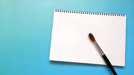 White blank sketch pad with a large water color brush, on a vibrant blue background.