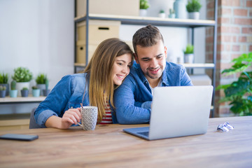 Young couple relaxing drinking a coffee and using the computer laptop around cardboard boxes, very happy moving to a new house