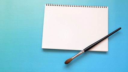 White blank sketch pad with a large water color brush, on a vibrant blue background.
