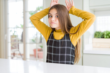Young beautiful blonde kid girl wearing casual yellow sweater at home Doing bunny ears gesture with...