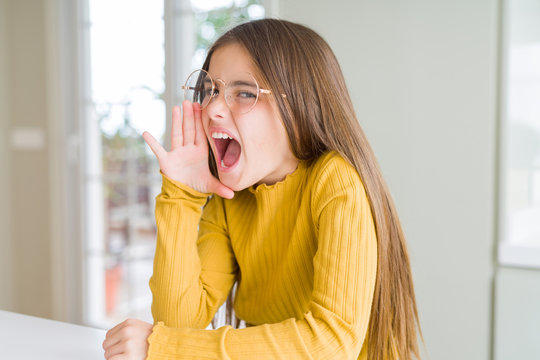 Beautiful young girl kid wearing glasses shouting and screaming loud to side with hand on mouth. Communication concept.