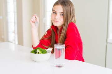 Beautiful young girl kid eating fresh broccoli and drinking water with a confident expression on smart face thinking serious