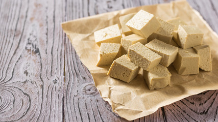 Pieces of tofu cheese on a piece of paper on a wooden table. Soy cheese.