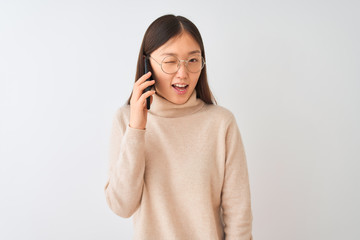 Young chinese woman talking on the smartphone over isolated white background winking looking at the...