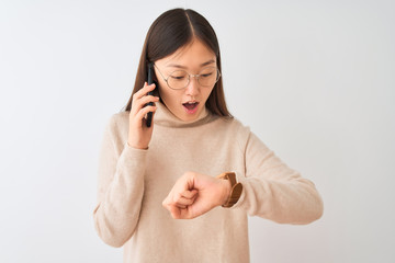 Young chinese woman talking on the smartphone over isolated white background Looking at the watch time worried, afraid of getting late