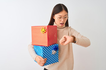 Young chinese woman holding birthday gifts over isolated white background Looking at the watch time...
