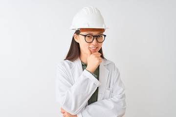 Young chinese engineer woman wearing coat helmet glasses over isolated white background looking confident at the camera smiling with crossed arms and hand raised on chin. Thinking positive.