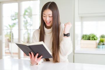 Beautiful Asian woman reading a book screaming proud and celebrating victory and success very excited, cheering emotion