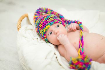 Close portrait of adorable baby in knitted funny gnome hat lies on his back in basket