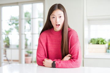 Beautiful Asian woman wearing pink sweater on white table afraid and shocked with surprise expression, fear and excited face.