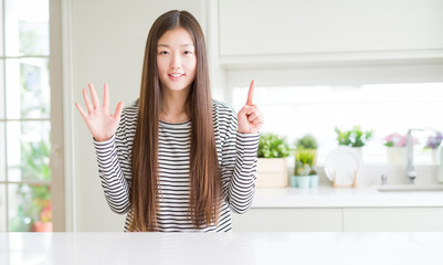 Beautiful Asian woman wearing stripes sweater showing and pointing up with fingers number six while smiling confident and happy.