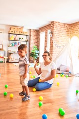 Fototapeta premium Beautiful teacher and toddler boy playing with colored small balls at kindergarten
