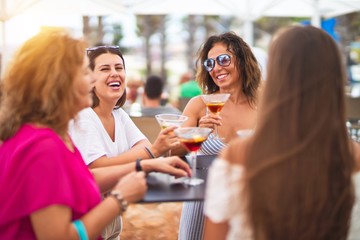 Beautiful group of women sitting at terrace of restaurant drinking cocktails speaking and smiling