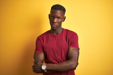 Young african american man wearing red t-shirt standing over isolated yellow background skeptic and...
