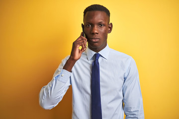 African american businessman talking on smartphone standing over isolated yellow background with a confident expression on smart face thinking serious