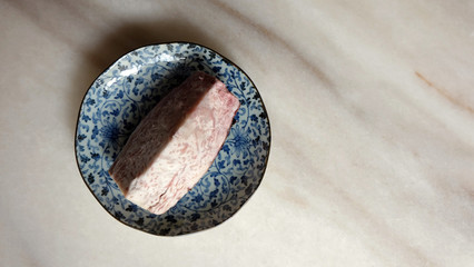 A large slice of steamed purple yam on a blue plate. Empty space on the right. Top view.