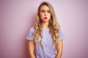 Young beautiful woman wearing purple t-shirt standing over pink isolated background puffing cheeks with funny face. Mouth inflated with air, crazy expression.