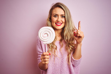 Young beautiful woman eating sweet candy over pink isolated background surprised with an idea or question pointing finger with happy face, number one