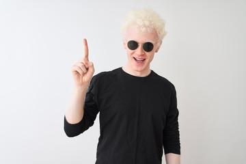 Naklejka premium Young albino man wearing black t-shirt and sunglasess standing over isolated white background pointing finger up with successful idea. Exited and happy. Number one.