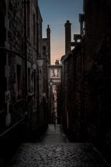 Naklejka na ściany i meble Narrow European alley, surrounded by bricks and cobblestone. Illuminated only with weak light from sunrise. Concept of scared or being alone and frightened