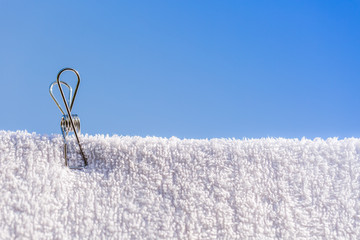 single stainless steel wire peg on a white towel with blue sky background