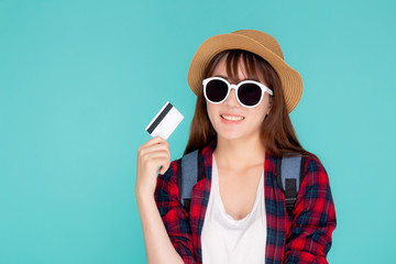 Beautiful young asian woman wear hat and sunglasses standing with showing credit card to travel summer trip isolated on blue background, asia girl journey in vacation with payment finance on card.