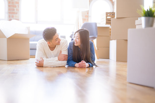 Young asian couple lying on the floor of new house arround cardboard boxes relaxing and smiling happy