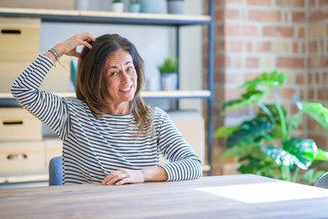 Middle age senior woman sitting at the table at home confuse and wonder about question. Uncertain with doubt, thinking with hand on head. Pensive concept.