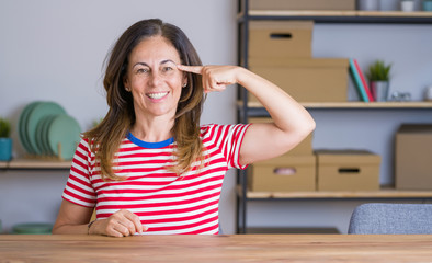 Middle age senior woman sitting at the table at home Smiling pointing to head with one finger, great idea or thought, good memory