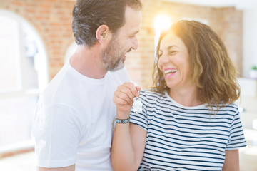 Middle age senior romantic couple holding and showing house keys smiling happy for moving to a new home