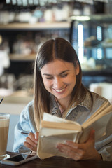 Young girl sitting in a cafe and reading a book