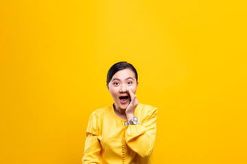 Woman make gossip gesture isolated over yellow background